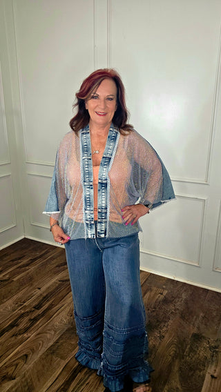 Woman wearing a sheer top over a plaid shirt with blue jeans indoors.