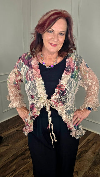 Woman wearing a floral lace cardigan over a dark top indoors.