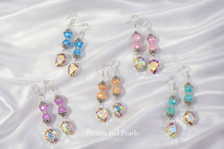 Colorful beaded earrings on a beige fabric background with 'Pirates and Pearls Boutique' branding.