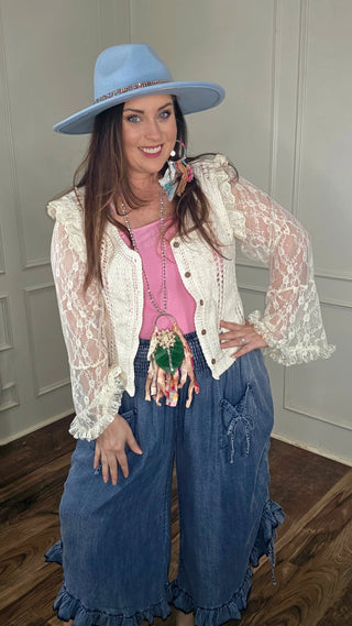 Woman wearing a white lace top, blue jeans, and a blue hat indoors.