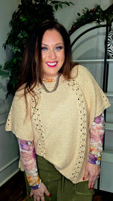 Woman wearing a beige knitted poncho with colorful sleeves indoors.